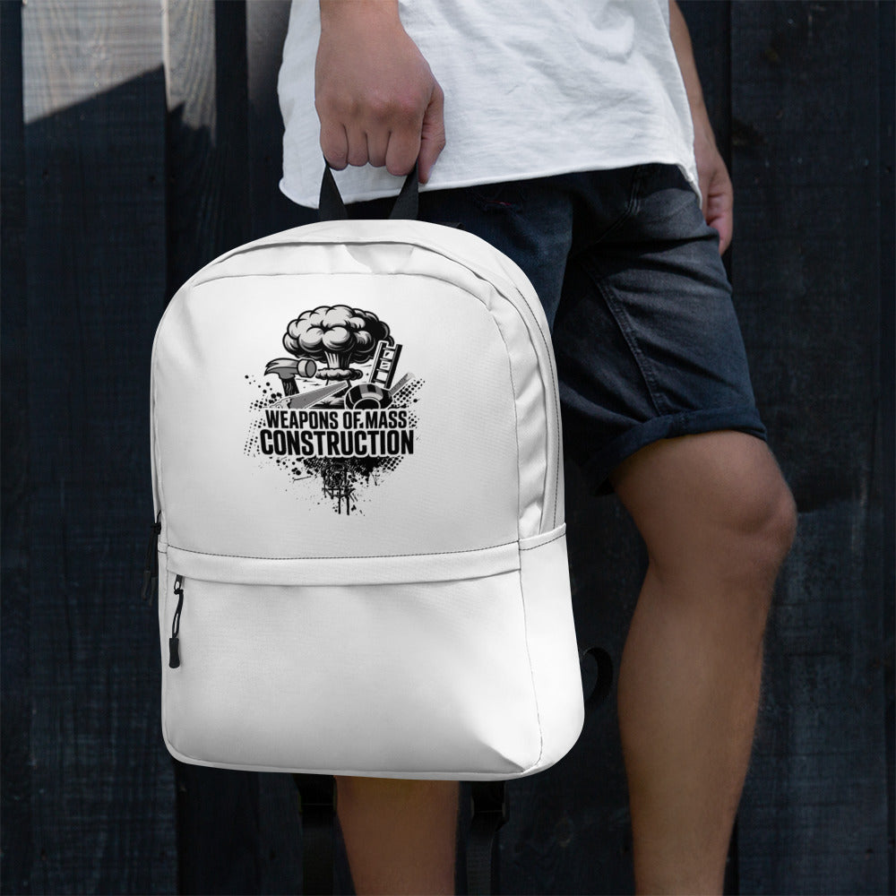 White backpack with 'Weapons of Mass Construction' design held by a person against a dark background