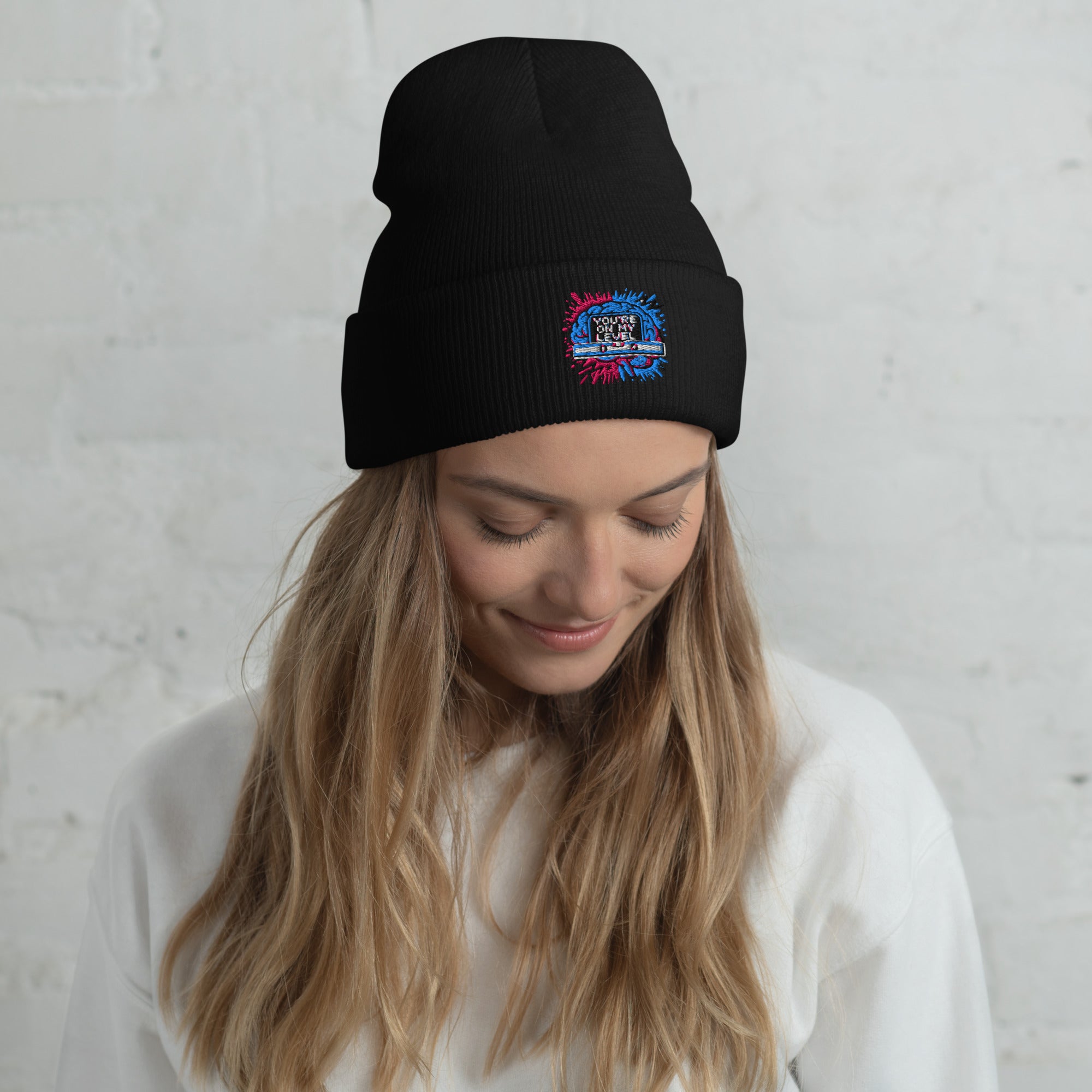 Person wearing a black beanie with a colorful logo against a light gray background