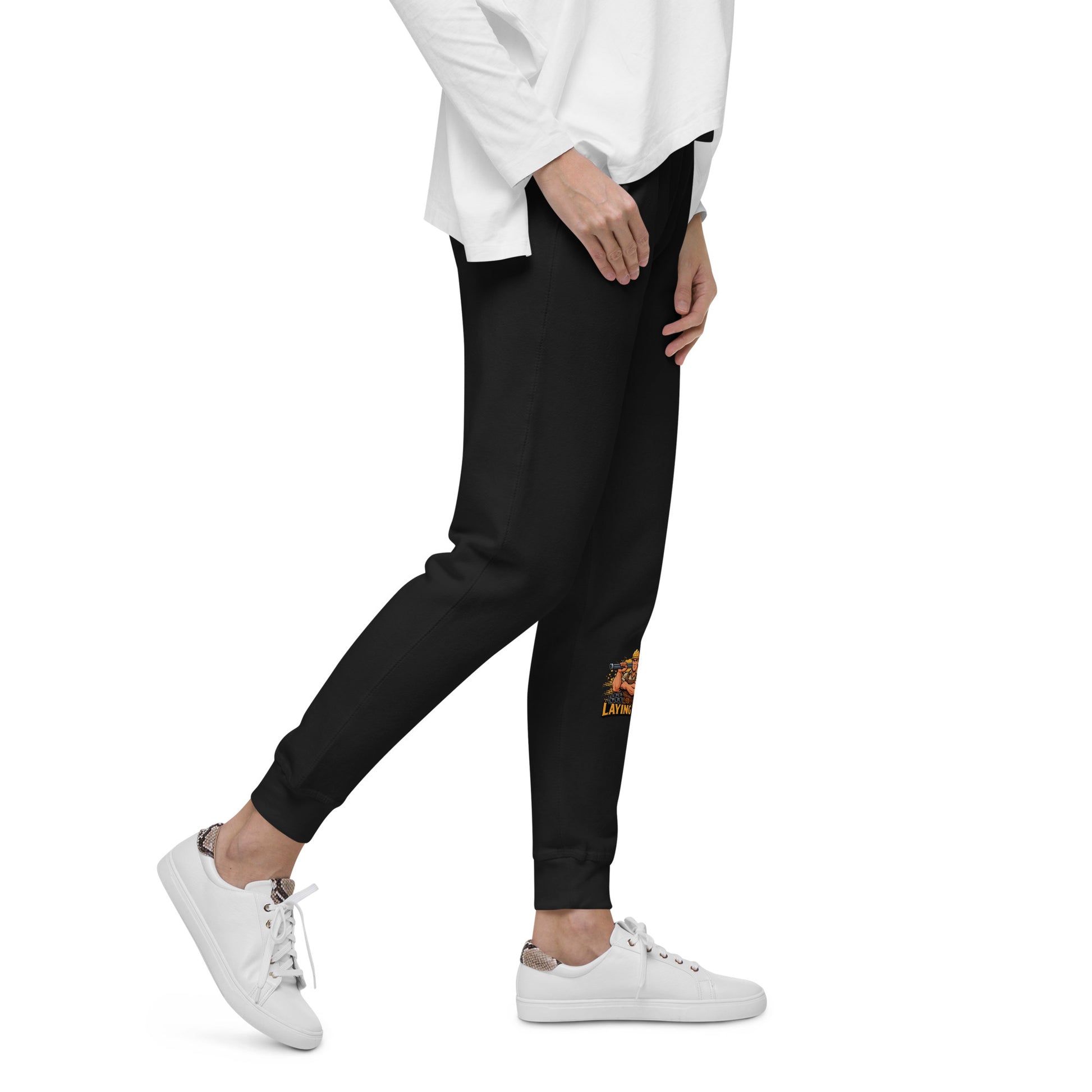 Person wearing black jogger pants with a logo and white sneakers on a white background